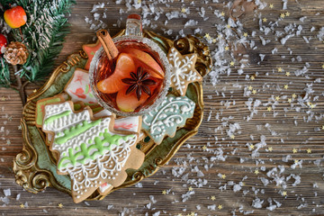 Mulled wine in a glass goblet with mandarin slices, cinnamon stick, apple slices and anise star on a beautiful wooden tray next to gigngerbreads in form of Cristmass tree and snowflake, top view