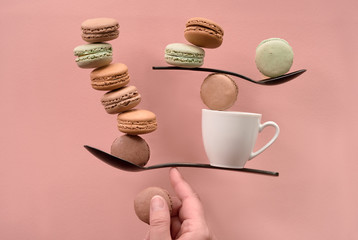 Fototapeta na wymiar Equilibrium concept flat lay on coral color paper with macarons and spoons
