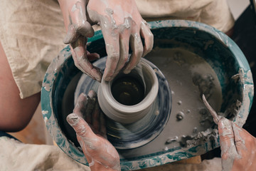 Man and woman hands pottery studying in studio. Creating vase. Hands in the clay and the potter's wheel with the product. Pottery class from above.