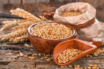 Wheat in a bag, bowl and wooden scoop on an old, rustic wooden surface