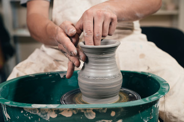 Young man making ceramic pot on the pottery wheel. Creating potter working on the wheel shaping clay making vase.