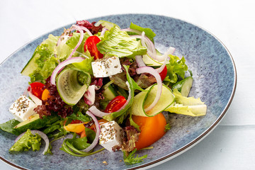 Classic Greek salad of tomatoes, cucumbers, red pepper, onions with olives, oregano and feta cheese. On a decorative plate