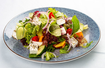 Classic Greek salad of tomatoes, cucumbers, red pepper, onions with olives, oregano and feta cheese. On a decorative plate