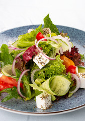 Classic Greek salad of tomatoes, cucumbers, red pepper, onions with olives, oregano and feta cheese. On a decorative plate