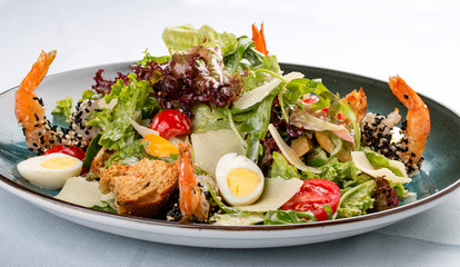 Fresh caesar salad on white bowl with parmesan cheese and shrimps. In a decorative plate