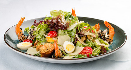 Fresh caesar salad on white bowl with parmesan cheese and shrimps. In a decorative plate
