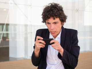 Displeased concerned businesswoman staring at cell phone screen near office building. Stressed nervous short haired young woman using smartphone near office building. Bad news concept