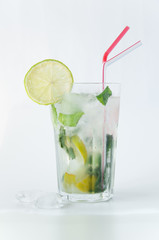 Mojito cocktail in a transparent glass with ice. Recipe for exotic drinks with mint, lime and white rum. Glass with a cocktail on a white background in the rays of the sun.
