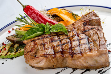 Tender grilled steak or T-bone steak served with grilled vegetables on a white plate.