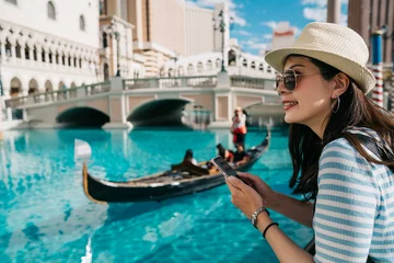 Fotobehang Toeristische vrouw reizen in Italië. Uitzicht op het Canal Grande met een gondelboot die vaart en erop beweegt. Jong meisje met strohoed en zonnebril glimlachend met behulp van mobiele telefoon terwijl u geniet van het uitzicht in Venetië. © PR Image Factory