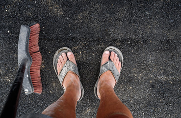 man in dirty feet in slippers standing on asphalt with sweep broom