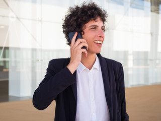 Happy confident androgynous businesswoman talking on cell outside. Smiling short haired young woman...