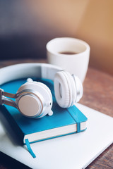 Necessary items. Headphones, cup of coffee, notebook and laptop on the table against defocused background. Copy space in upper part