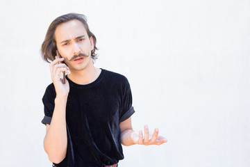 Unnerved young man with handlebar mustache talking on phone. Closeup shot of stylish thoughtful guy with smartphone. Communication and technology concept