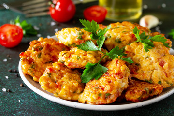 Chicken cutlets made from minced meat close-up, with paprika, tomatoes and greens in a bowl on a dark stone table.