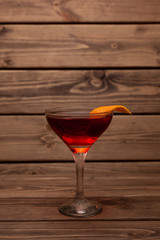 Red alcoholic cocktail in a shot glass on a totally wooden background: homemade bitter berry tincture with a slice of orange peel