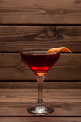 Red alcoholic cocktail in a shot glass on a totally wooden background: homemade bitter berry tincture with a slice of orange peel