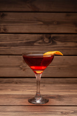 Red alcoholic cocktail in a shot glass on a totally wooden background: homemade bitter berry tincture with a slice of orange peel