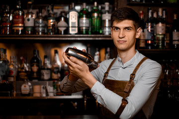 Attractive male bartender holding in hands a steel shaker