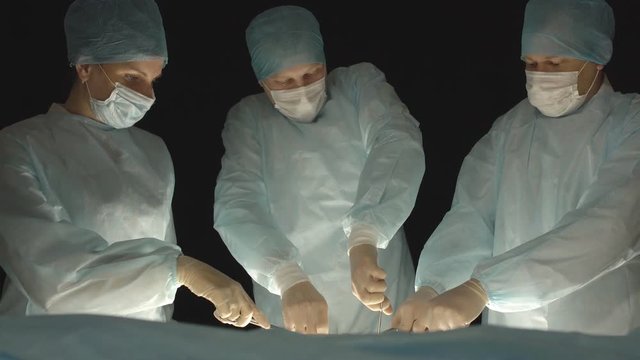 Three surgeons, a man and a woman, perform surgery in the operating room to remove and transplant human organs, resect the stomach and remove the gallbladder, appendicitis
