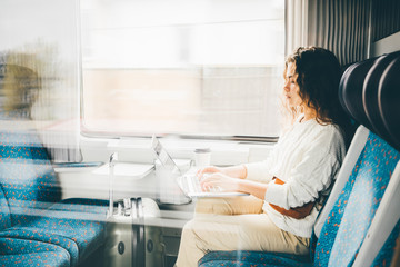 Freelancer girl in white sweater working with laptop in the train, business travel or technology...
