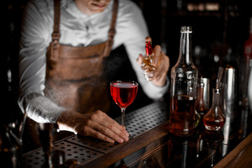 Professional bartender spraying on the red alcoholic cocktail