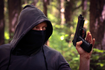 Man in hood with the pistol in the forest.
