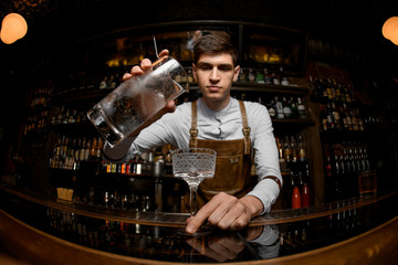Fisheye shot male bartender pouring a cocktail from the measuring cup to the glass