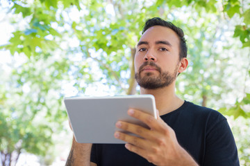 Bearded man using tablet pc outdoor. Low angle view of handsome young man holding digital tablet. Wireless technology concept