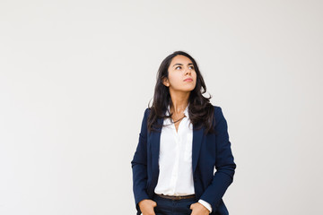 Confident businesswoman with hands in pockets looking up. Professional confident young businesswoman standing with hands in pockets isolated on grey background. Business concept - Powered by Adobe