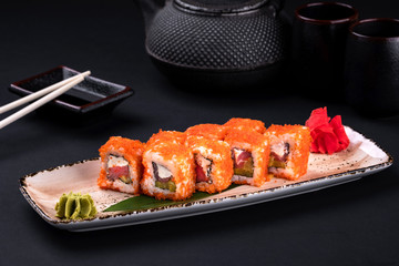 Close up of sashimi sushi set with chopsticks with shrimp, cucumber and cheese philadelphia and soy on black background. California rolls and green tea teapot, copy space. Japanese food.