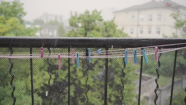 Some colorful clothespins hang on the washing line in the pouring rain. Slow motion