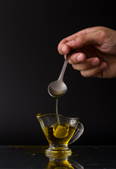  hold with olive spoon with glass bowl with extra virgin olive oil on black background