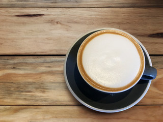 Hot cappuccino coffee in blue cup on wooden table background. Art of milk foam circle shape with copy space on brown melt coffee top view