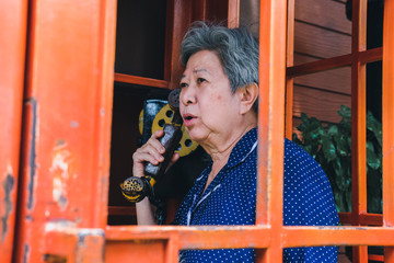 Fototapeta na wymiar old elderly senior woman talking on vintage public telephone