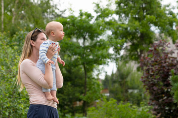 Obraz premium Cute baby boy in mother's arms. Exited baby gets acquainted with birds in countryside. Vacation in a summer residence in a rural countryside. 