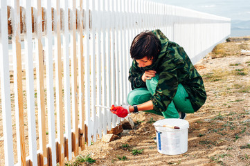 Beautiful girl paints a wooden fence with a brush