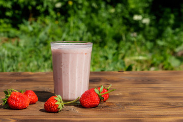 Glass of fresh strawberry smoothie on a wooden table outdoor