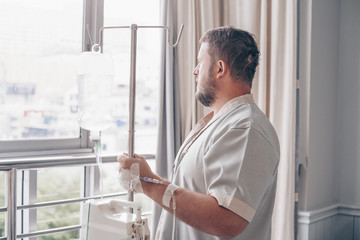 Fototapeta premium A man stands in a hospital ward and looks out the window. Dropper in a mans hand in a hospital.