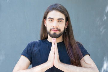 Handsome young brunet with piercing praying. Cheerful believer with long hair posing. Religion...