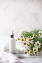 Obraz na płótnie Canvas Organic vegan natural cosmetics concept. Chamomile flowers and cosmetic bottles of cream and serum essential on white background. Zero waste cosmetic package