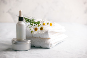 Chamomile flowers and cosmetic bottles of cream and serum essential on white background. Space for text. Zero waste cosmetic package concept