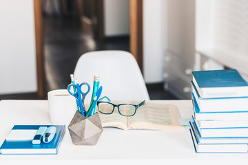 Modern stylish office work place with open book, glasses, office supplies and books, desk work concept in white and blue colors.