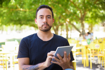 Handsome man holding tablet pc and looking at camera. Bearded young man using digital tablet outdoor. Wireless technology concept