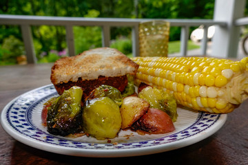 Cornwall, Connectcut, USA A plate of grilled potatoes and brussel sprouts with corn on the cob and an Impossible vegetarian burger.