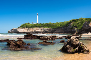 Clear water and rocks on the beach in Biarritz with the lighthouse. Basque Country of France.