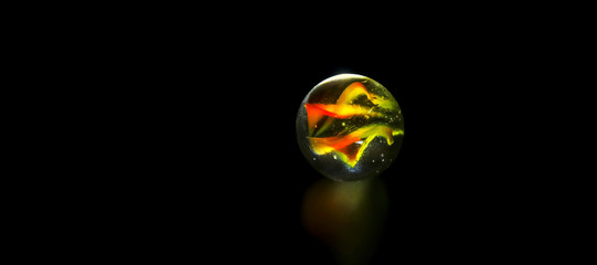 A shiny colorful marble ball speckled in surface reflection with full black background view.