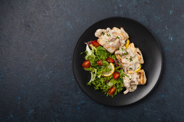 Fried cod served with mushroom sauce and salads. Portion on a black plate. Dark background.