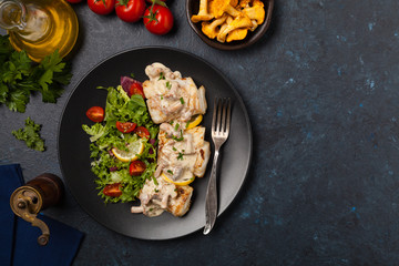 Fried cod served with mushroom sauce and salads. Portion on a black plate. Dark background.