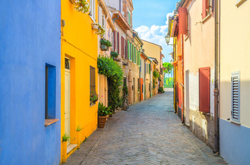 Fototapeta na wymiar Typical italian cobblestone street with colorful multicolored buildings, traditional houses with green plants on walls and shutter windows in old historical city centre Rimini, Emilia-Romagna, Italy